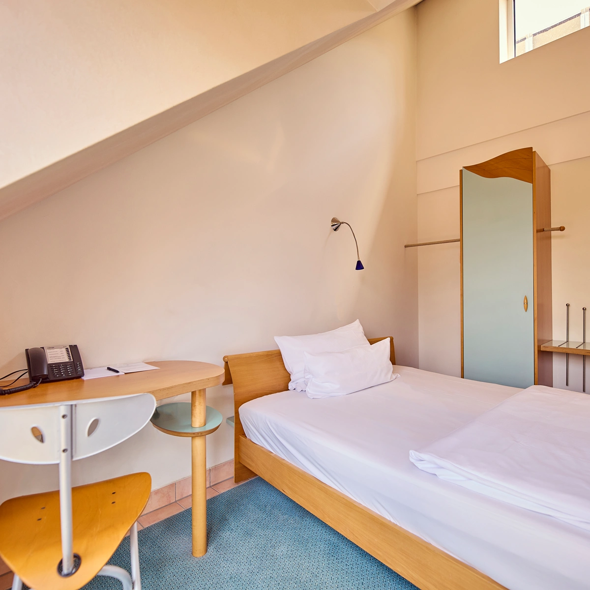 hotel-watthalden-watthaldenzimmer03 Blick in ein Watthaldenzimmer mit Einzelbett, Schreibtisch, Stuhl und Stauraum.